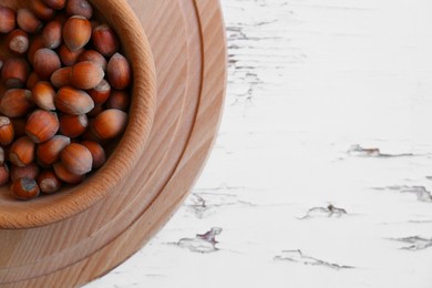 Photo of Bowl with hazelnuts on white wooden table, top view. Space for text