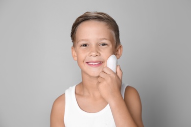 Photo of Cute little boy with soap bar on gray background