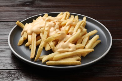 Photo of Delicious french fries with cheese sauce on wooden table, closeup