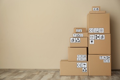 Photo of Cardboard boxes with different packaging symbols on floor near beige wall, space for text. Parcel delivery