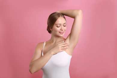 Photo of Young woman with smooth clean armpit on pink background. Using deodorant