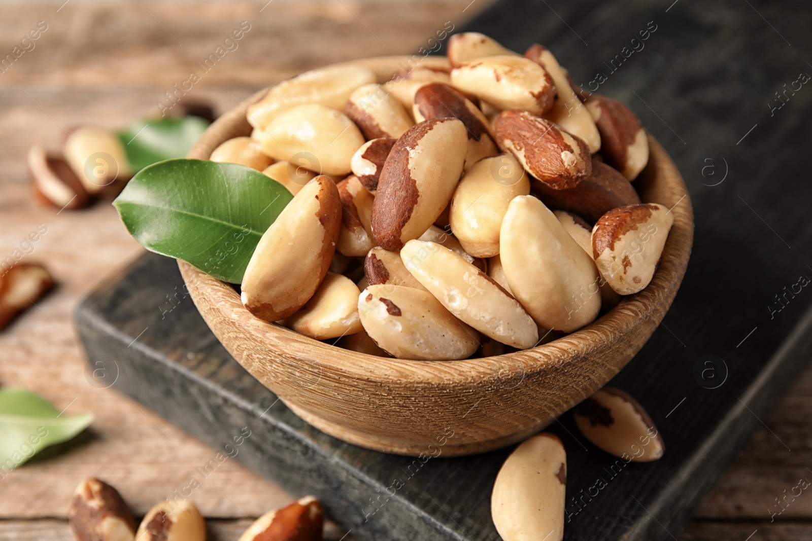 Photo of Wooden board with bowl of tasty Brazil nuts on table