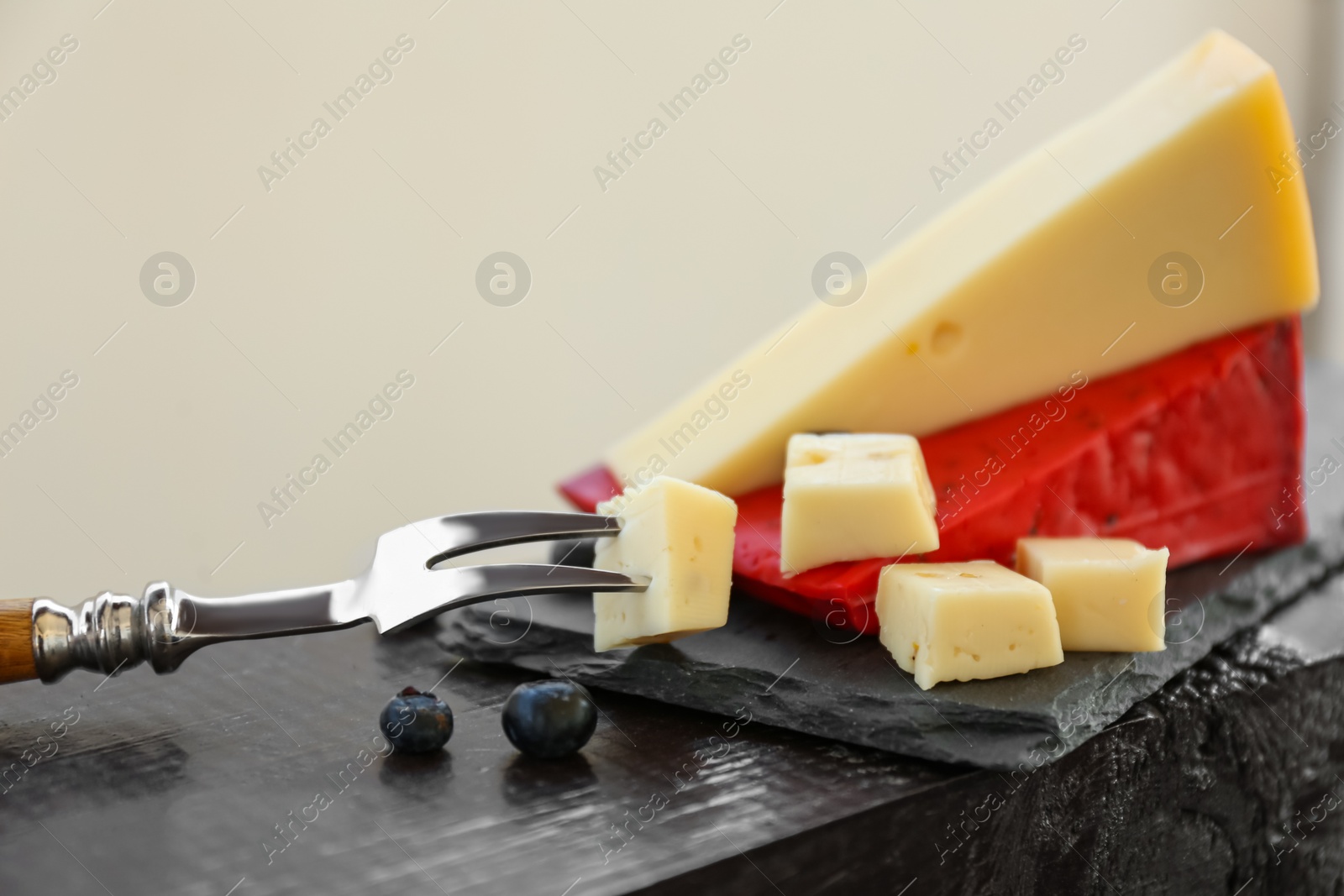 Photo of Different delicious cheeses, fork and blueberries on slate plate, closeup