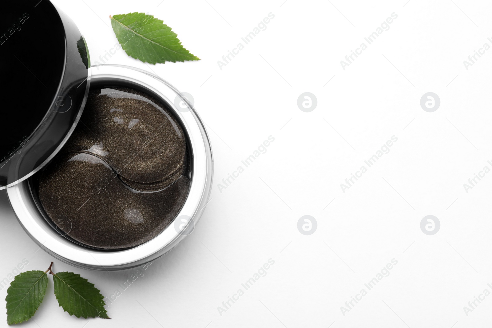 Photo of Under eye patches in jar and green leaves on white background, flat lay. Space for text