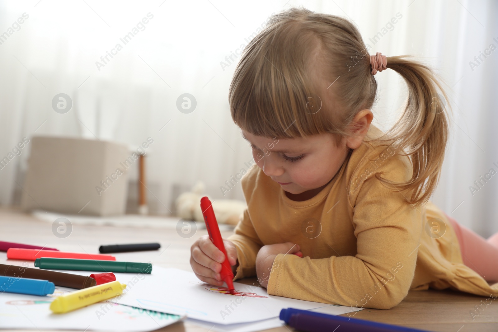 Photo of Cute little girl drawing with marker on floor indoors. Child`s art