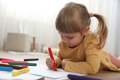 Photo of Cute little girl drawing with marker on floor indoors. Child`s art