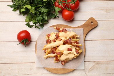 Photo of Delicious French fries with bacon, cheese sauce, tomatoes and herbs on wooden table, flat lay