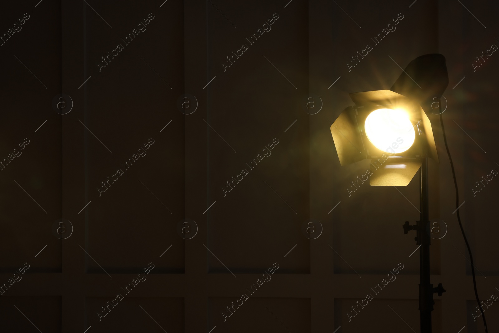 Photo of Bright yellow spotlight near wall in dark room, space for text