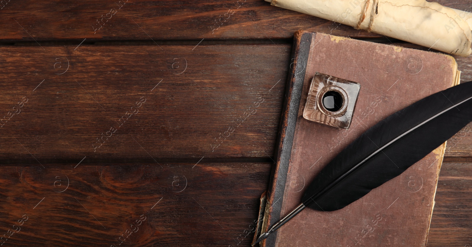 Image of Quill, inkwell, old book and parchment scroll on wooden table, flat lay with space for text. Banner design