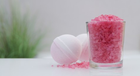 Photo of Glass with sea salt and bath bombs on table in bathroom, closeup. Space for text