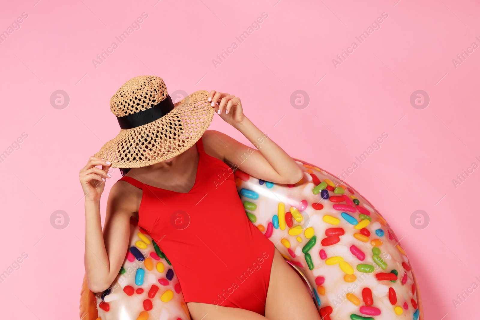 Photo of Young woman in stylish swimsuit on inflatable ring against pink background, top view