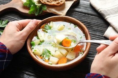 Photo of Woman eating fresh homemade vegetable soup at wooden table, closeup