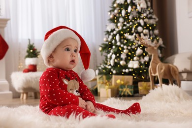 Baby in Santa hat and bright Christmas pajamas on floor at home