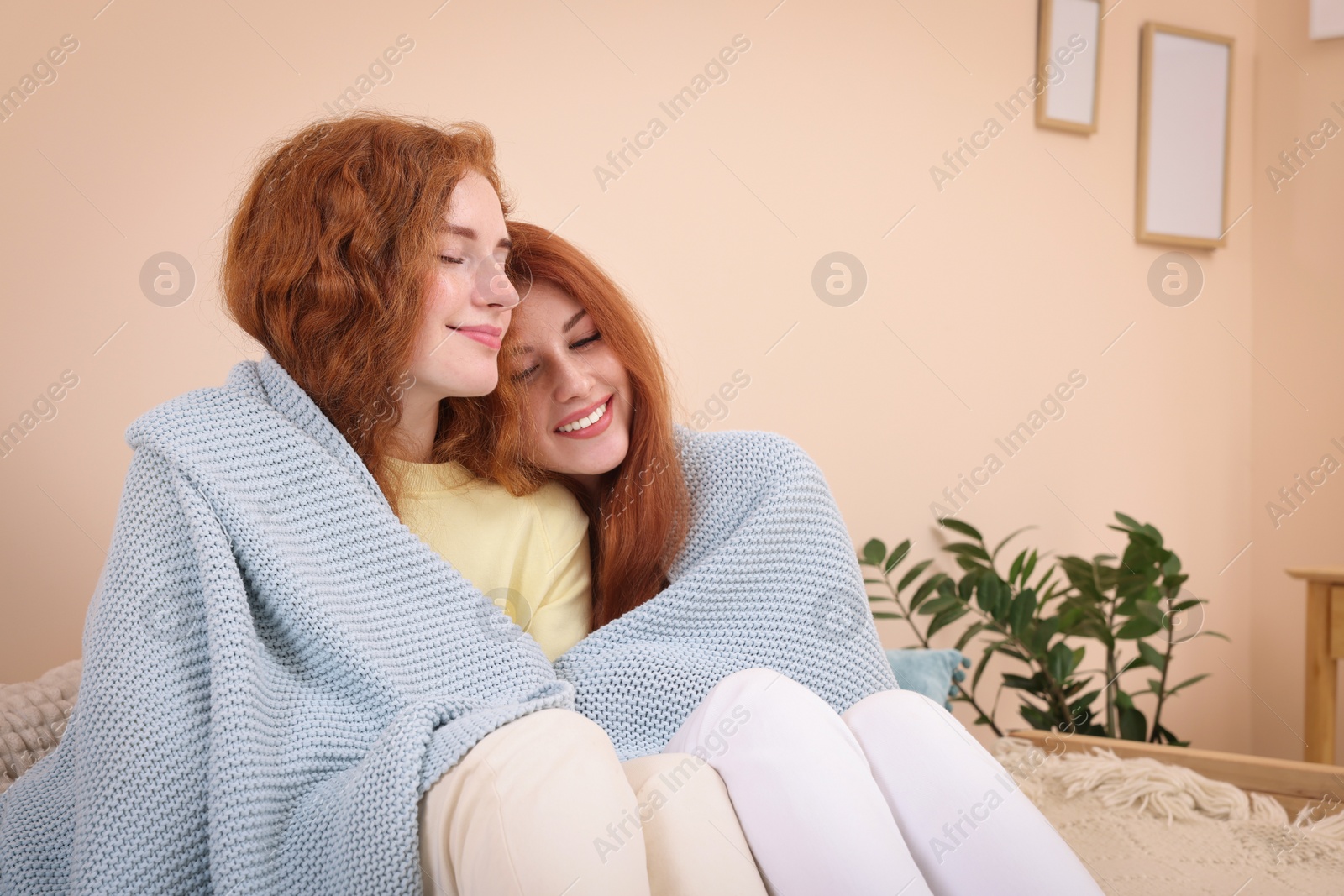 Photo of Portrait of beautiful young redhead sisters wrapped in plaid at home. Space for text