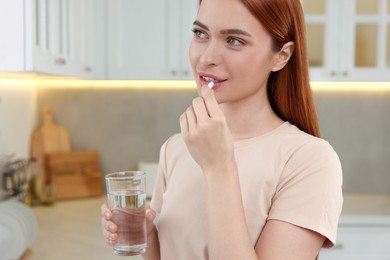 Photo of Beautiful young woman taking vitamin pill at home