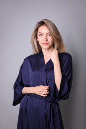 Photo of Pretty young woman in beautiful dark blue silk robe on grey background