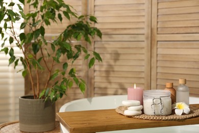 Photo of Wooden tray with spa products, stones and burning candle on bath tub in bathroom. Space for text