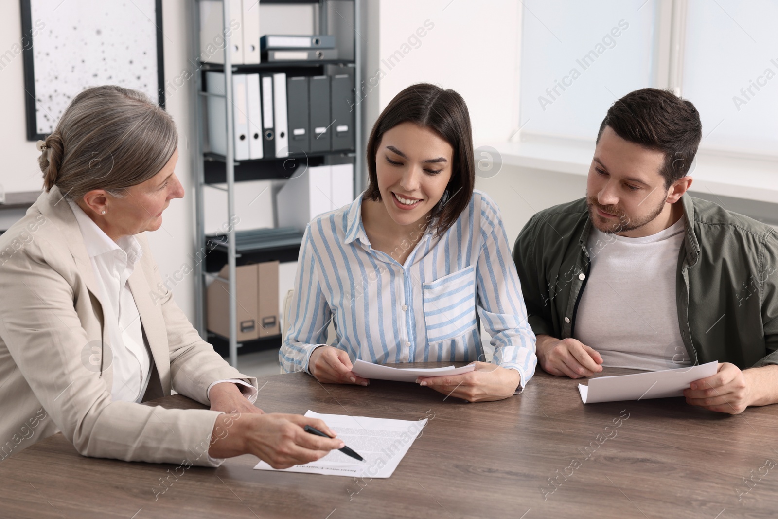 Photo of Young couple consulting insurance agent about pension plan at wooden table indoors