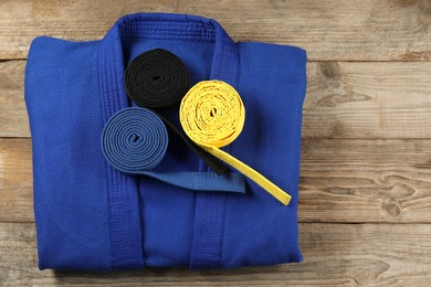 Photo of Karate belts and blue kimono on wooden background, top view. Space for text
