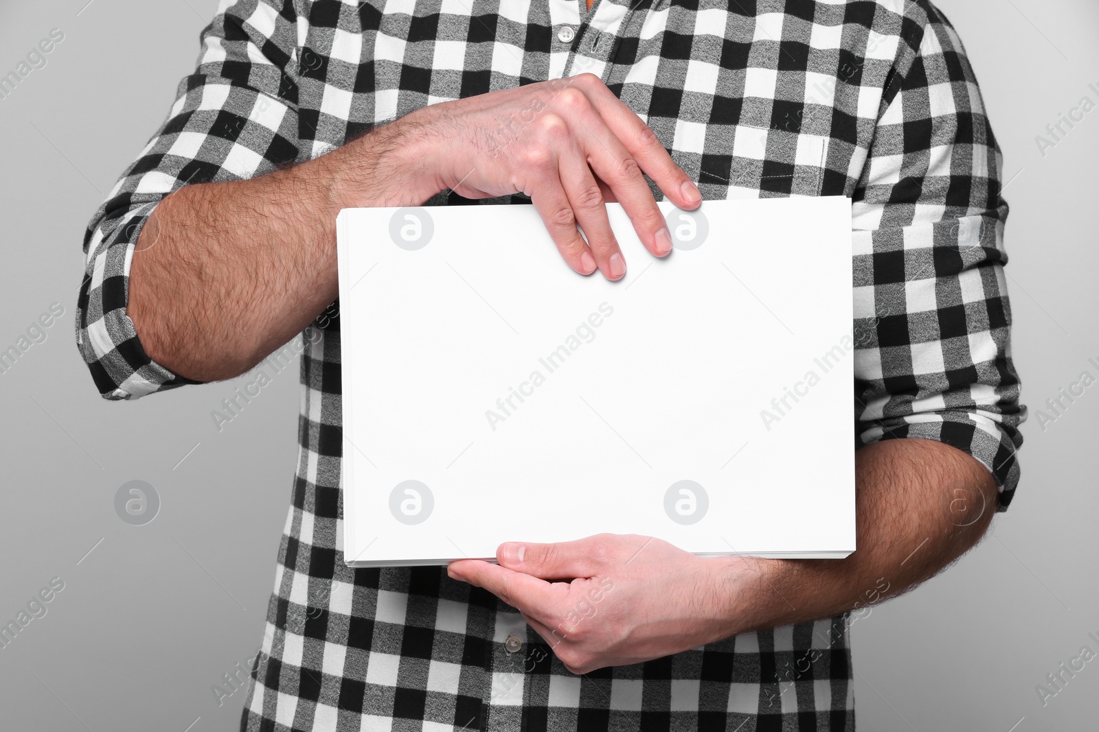 Photo of Man holding sheet of paper on light grey background, closeup. Mockup for design