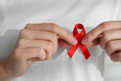 Photo of Woman holding red awareness ribbon, closeup. World AIDS disease day