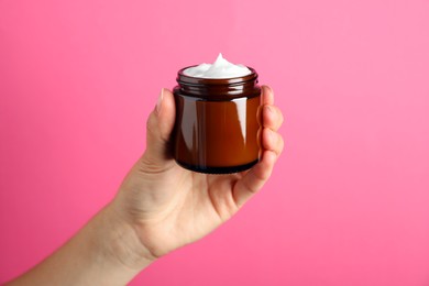 Photo of Woman holding jar of face cream on pink background, closeup