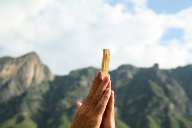 Photo of Man holding palo santo stick in high mountains, closeup