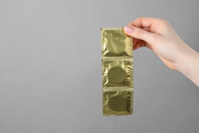 Woman holding condoms on grey background, closeup. Space for text