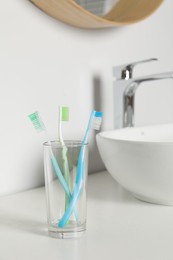 Photo of Plastic toothbrushes in glass holder on white countertop in bathroom