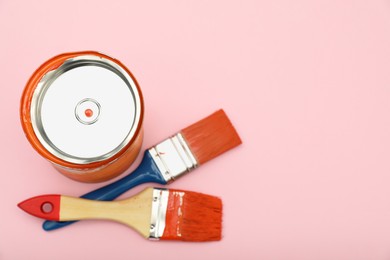 Photo of Can of orange paint and brushes on pink background, flat lay. Space for text