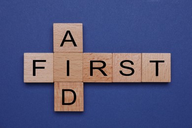 Photo of Words First Aid made of wooden cubes on blue background, top view