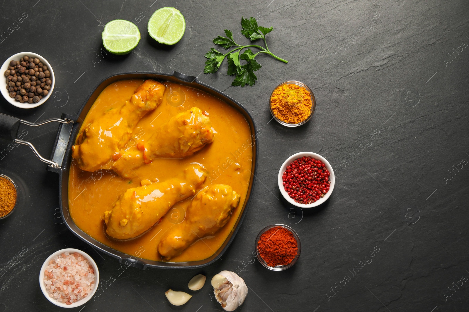 Photo of Tasty chicken curry and ingredients on black textured table, flat lay. Space for text