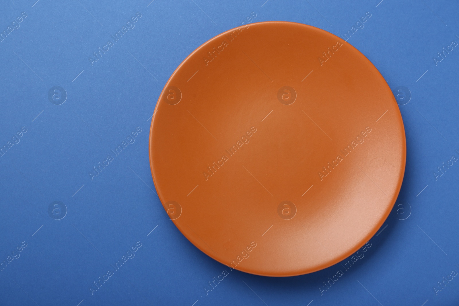 Photo of Empty orange ceramic plate on blue background, top view. Space for text