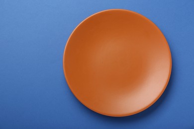 Photo of Empty orange ceramic plate on blue background, top view. Space for text