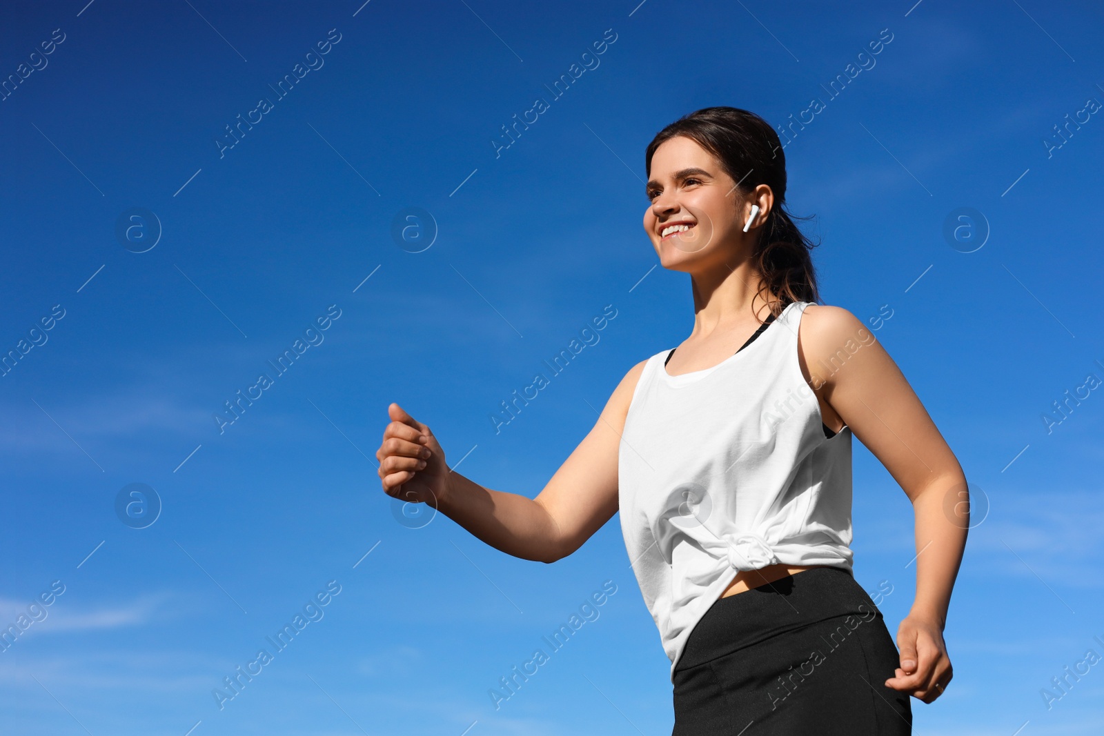 Photo of Young woman listening to music while running outdoors in morning, low angle view. Space for text