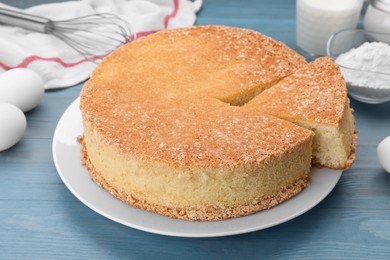 Photo of Tasty sponge cake and ingredients on light blue wooden table, closeup