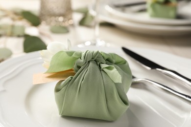 Photo of Furoshiki technique. Gift packed in green fabric with flower and blank card on plate, closeup