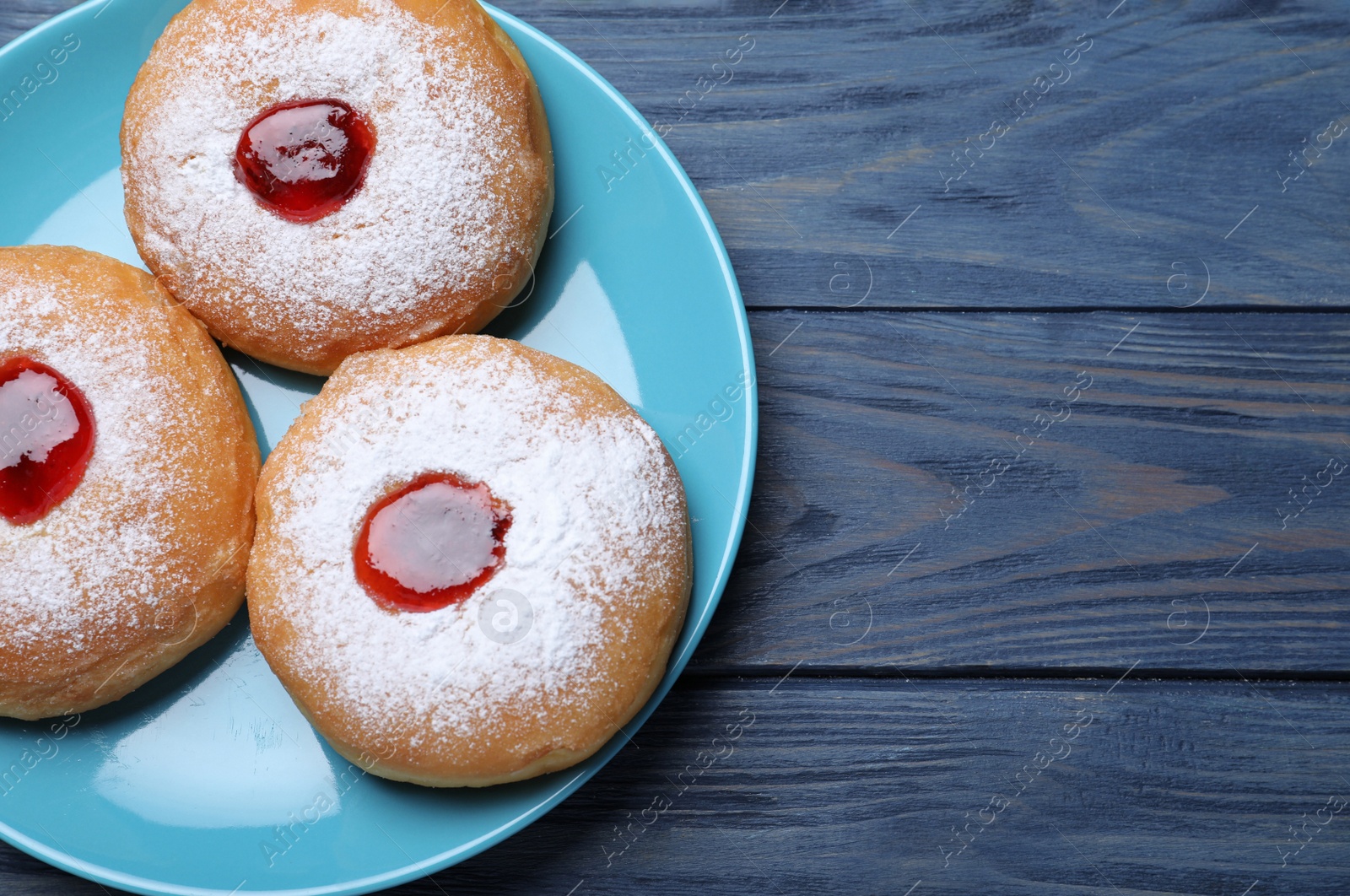 Photo of Hanukkah doughnuts with jelly and sugar powder on blue wooden table, top view. Space for text