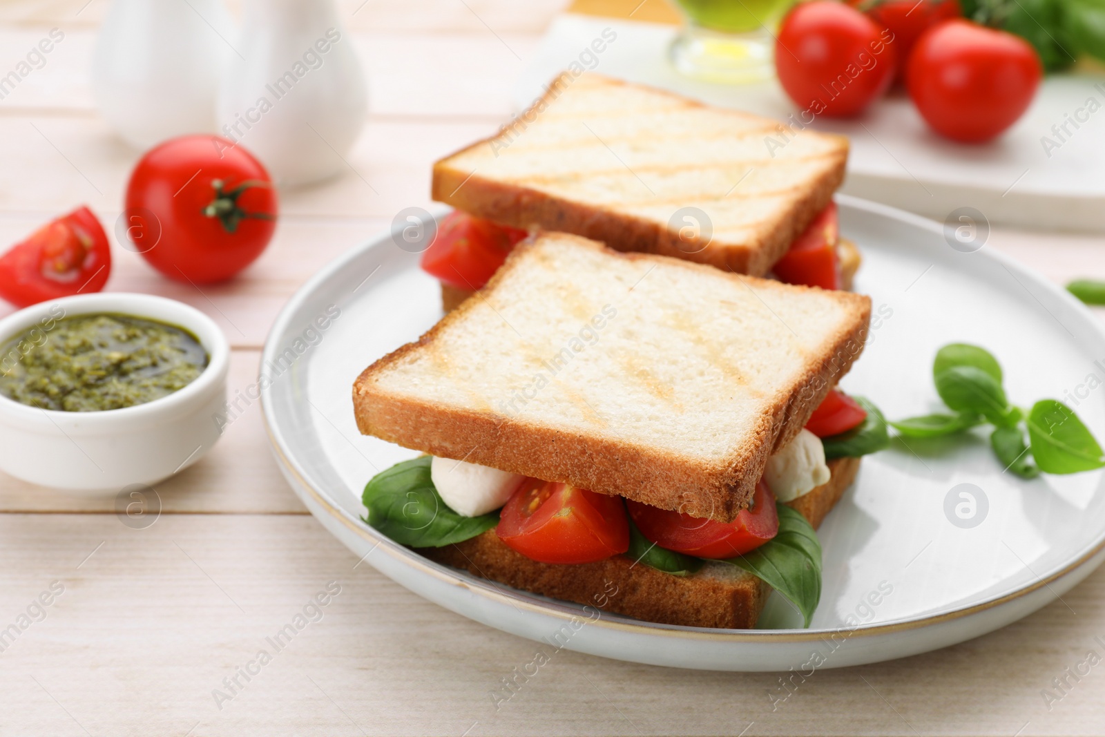 Photo of Delicious Caprese sandwiches with mozzarella, tomatoes, basil and pesto sauce on white wooden table