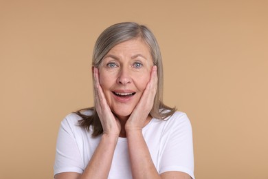 Photo of Portrait of happy surprised senior woman on beige background