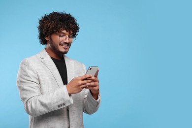 Photo of Handsome smiling man using smartphone on light blue background, space for text