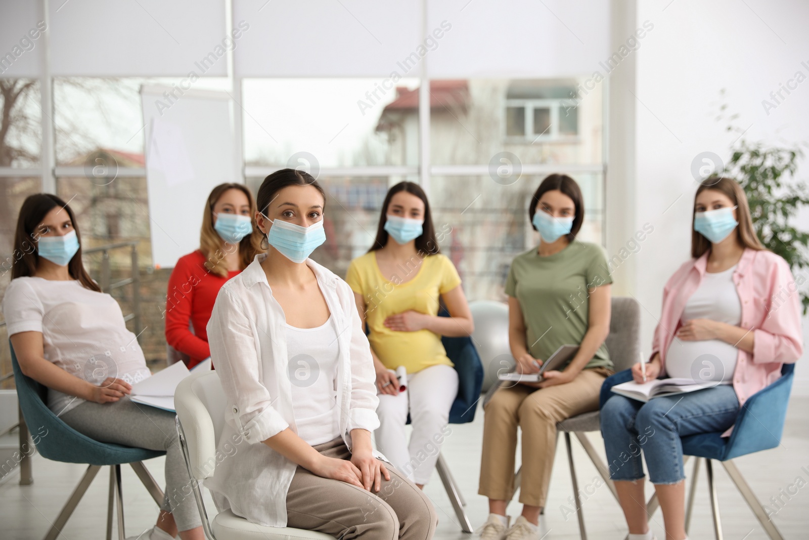 Photo of Group of pregnant women and midwife in protective masks at courses for expectant mothers indoors