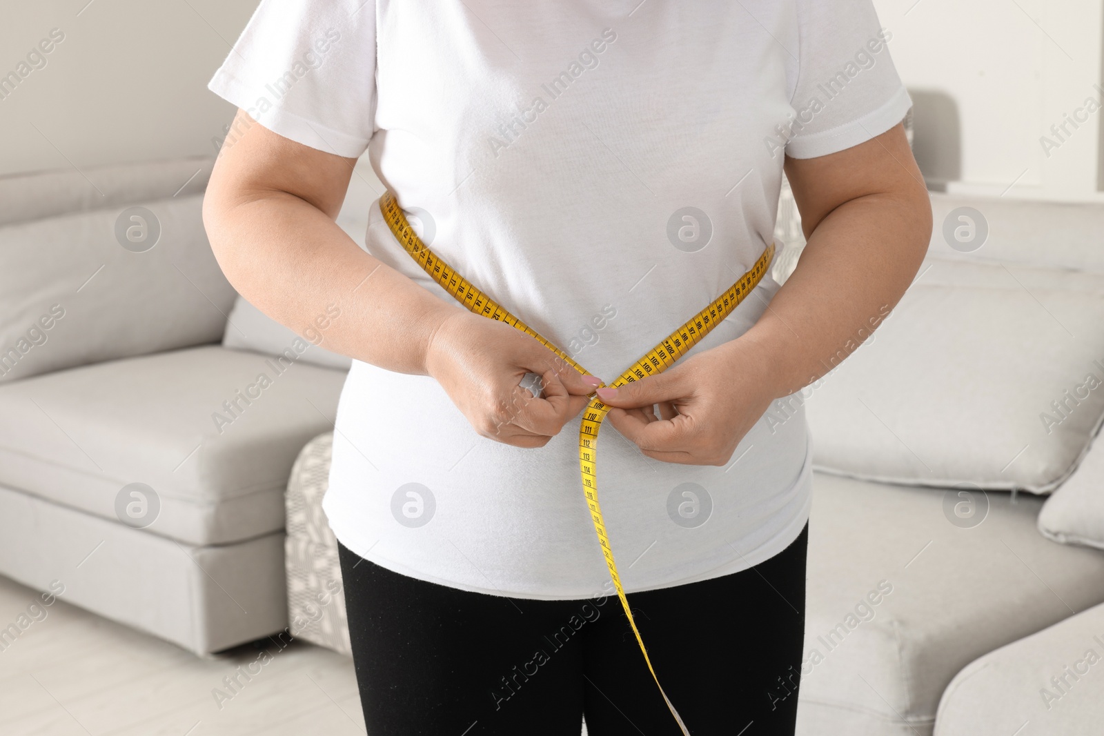 Photo of Overweight woman measuring waist with tape at home, closeup