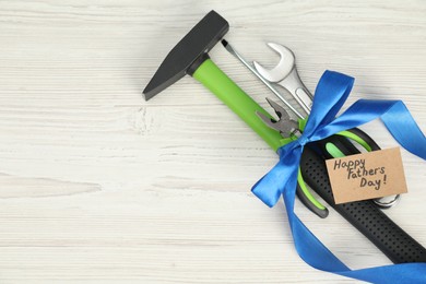 Photo of Happy Father's Day. Greeting card and set of tools tied with ribbon on light wooden table, top view. Space for text