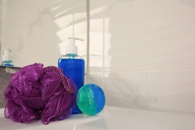 Photo of Purple shower puff and cosmetic products on sink in bathroom, space for text