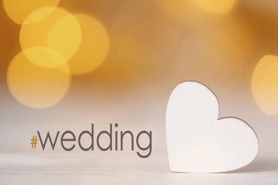 Image of Hashtag Wedding and white decorative heart on table. Bokeh effect