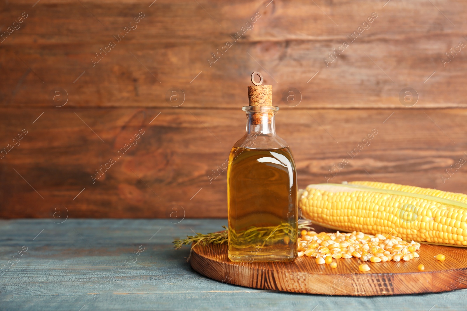 Photo of Bottle of corn oil and fresh cobs on table against wooden wall