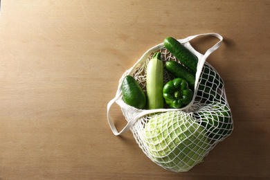 Photo of Different fresh vegetables in eco mesh bag on wooden table, top view