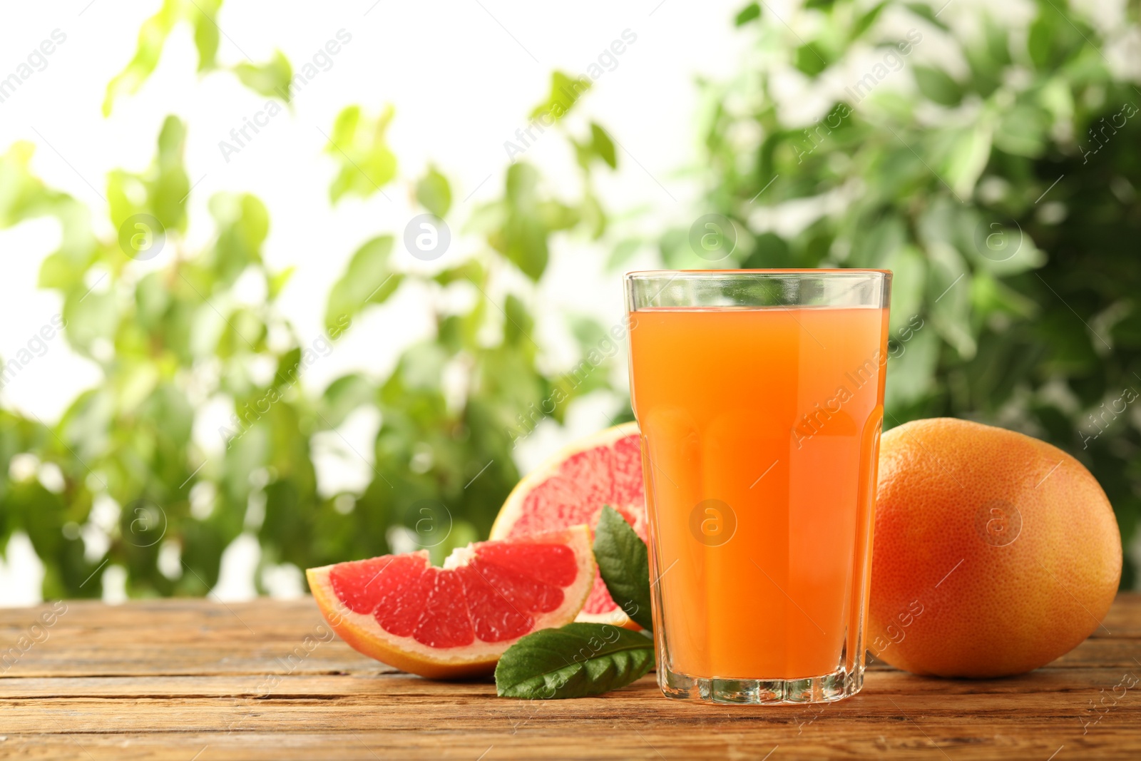 Photo of Glass of delicious grapefruit juice on wooden table against blurred background, space for text