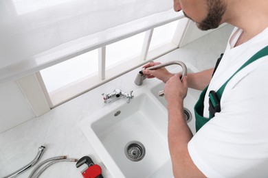 Photo of Professional plumber fixing water tap in kitchen, above view